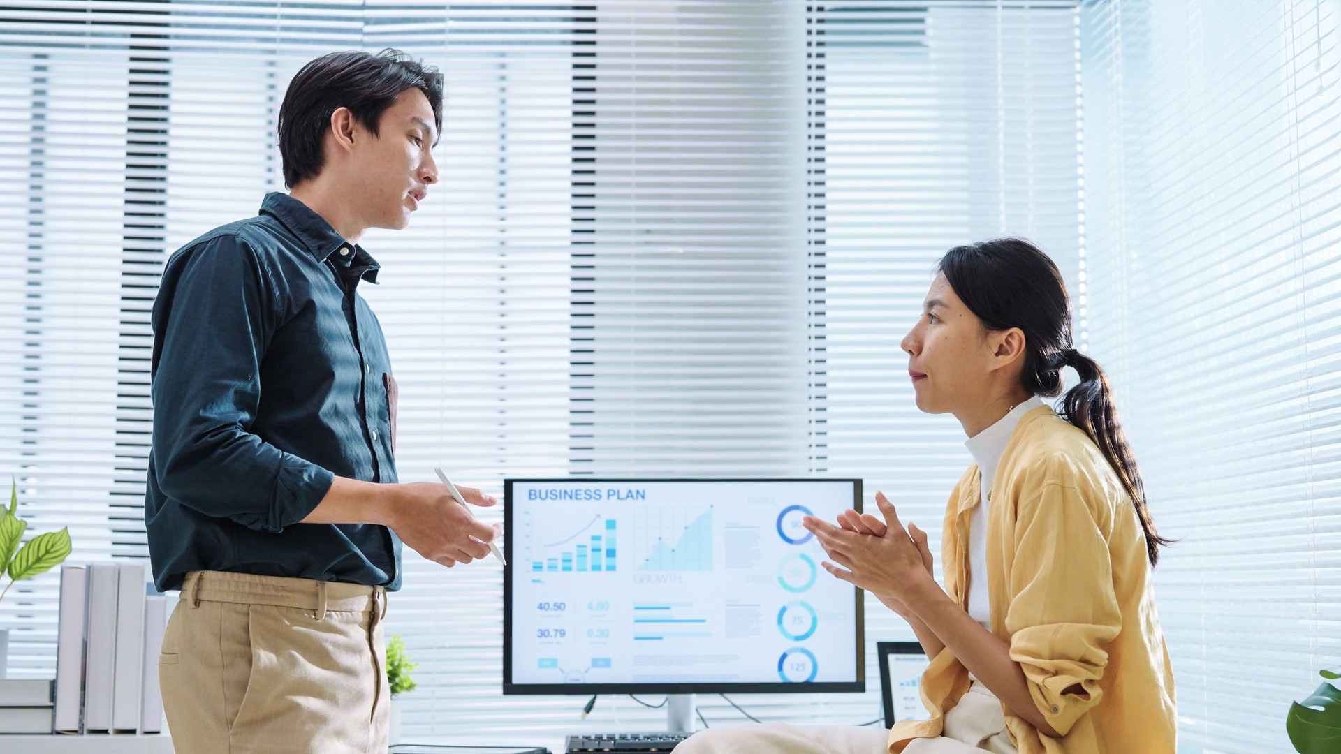 Two Asian business person working on laptop computer discuss and collaborate while analysis and reviewing information data marketing and trend in a modern office.